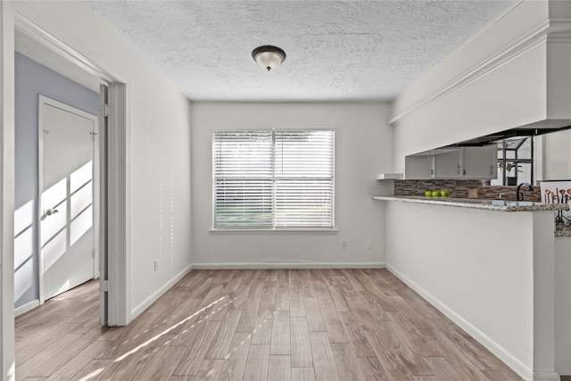 interior space with kitchen peninsula, backsplash, light hardwood / wood-style floors, and a textured ceiling