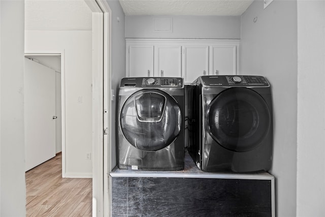 laundry room with cabinets, a textured ceiling, light wood-type flooring, and independent washer and dryer