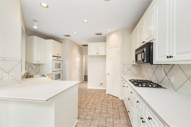 kitchen featuring white cabinets, kitchen peninsula, stainless steel gas cooktop, double oven, and sink