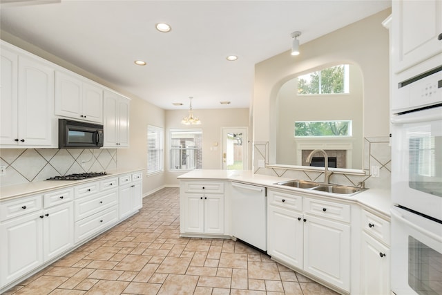 kitchen featuring white cabinets, white appliances, kitchen peninsula, pendant lighting, and sink