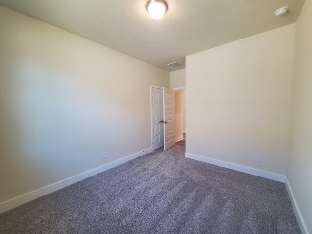 empty room featuring visible vents, dark carpet, and baseboards