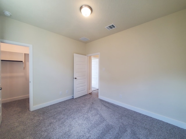 unfurnished bedroom with carpet, a walk in closet, visible vents, and baseboards