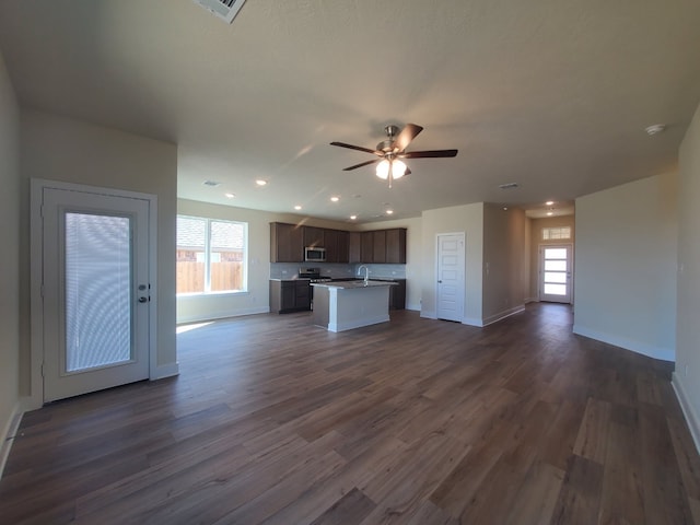 kitchen featuring ceiling fan, open floor plan, dark wood-style floors, stainless steel microwave, and an island with sink