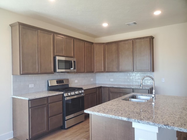 kitchen with visible vents, decorative backsplash, light stone counters, stainless steel appliances, and a sink