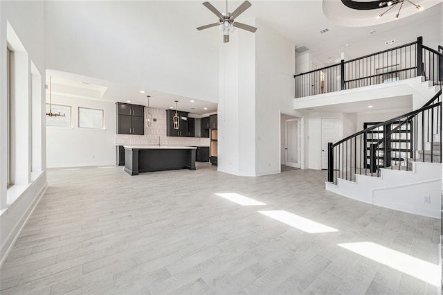 unfurnished living room featuring a high ceiling, ceiling fan, and light wood-type flooring