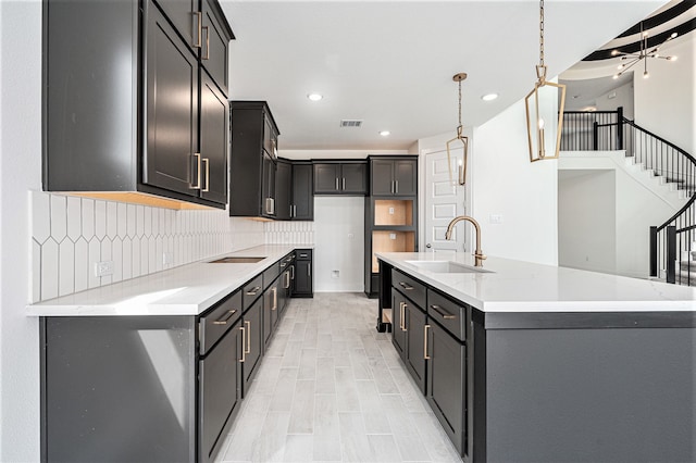 kitchen with backsplash, pendant lighting, a kitchen island with sink, sink, and a chandelier