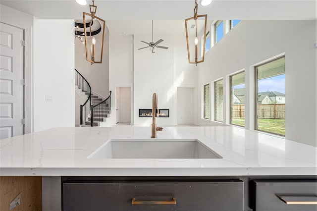 kitchen with light stone counters, sink, a center island with sink, ceiling fan, and stainless steel dishwasher