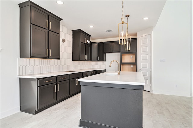 kitchen featuring pendant lighting, a chandelier, tasteful backsplash, sink, and a center island with sink