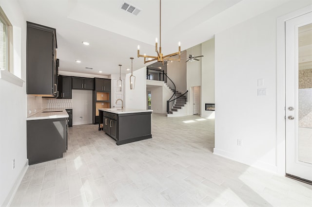 kitchen with tasteful backsplash, ceiling fan with notable chandelier, decorative light fixtures, a kitchen island with sink, and sink