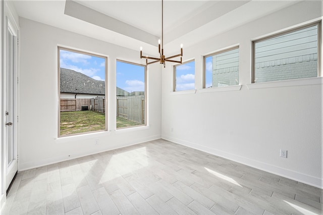 unfurnished room featuring a notable chandelier, light wood-type flooring, a tray ceiling, and a healthy amount of sunlight