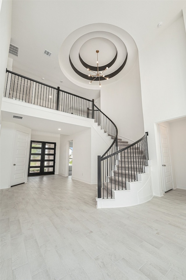 staircase featuring a towering ceiling, a chandelier, a raised ceiling, and hardwood / wood-style flooring