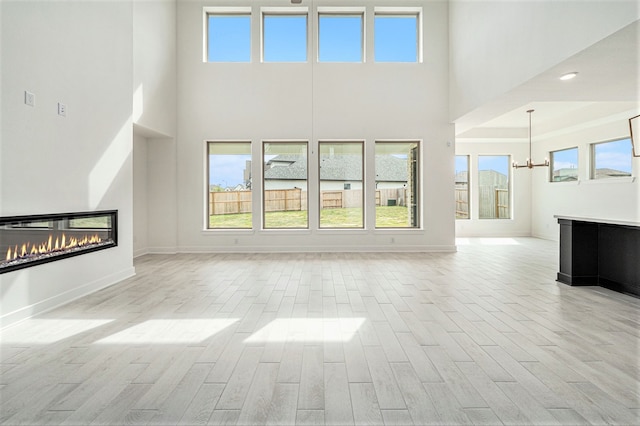 unfurnished living room featuring light hardwood / wood-style flooring, a high ceiling, and a healthy amount of sunlight