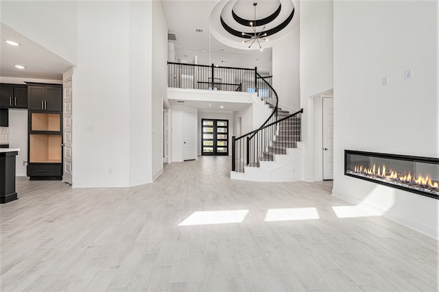 entryway with a notable chandelier, light wood-type flooring, a towering ceiling, and a raised ceiling