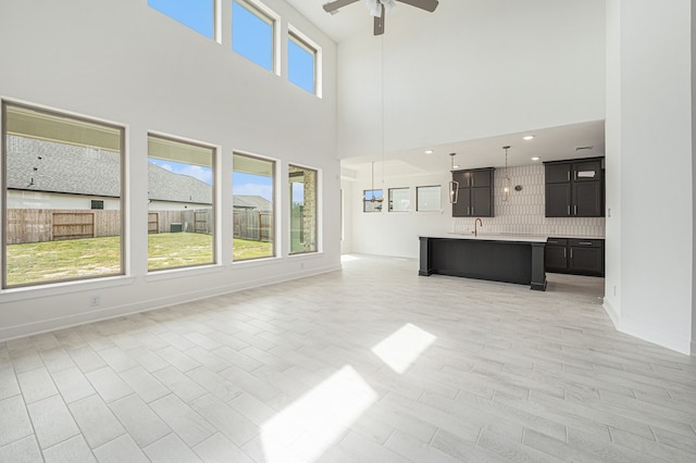 unfurnished living room featuring a high ceiling, sink, ceiling fan, and light hardwood / wood-style flooring