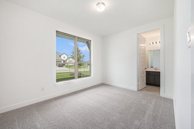 unfurnished bedroom with light colored carpet, ensuite bath, and sink