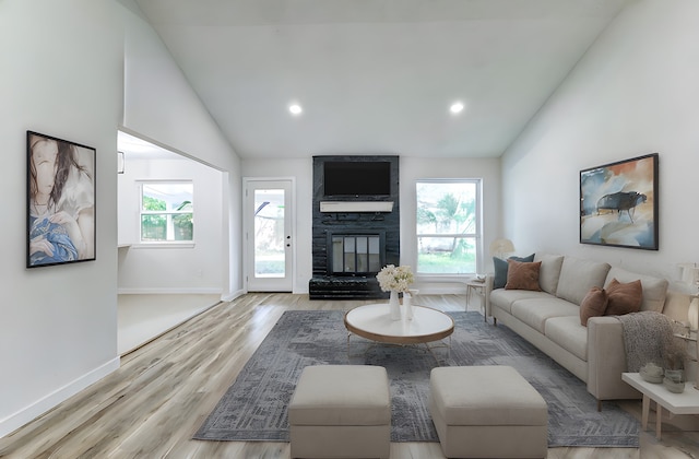 living room with light wood-type flooring, a healthy amount of sunlight, a stone fireplace, and high vaulted ceiling