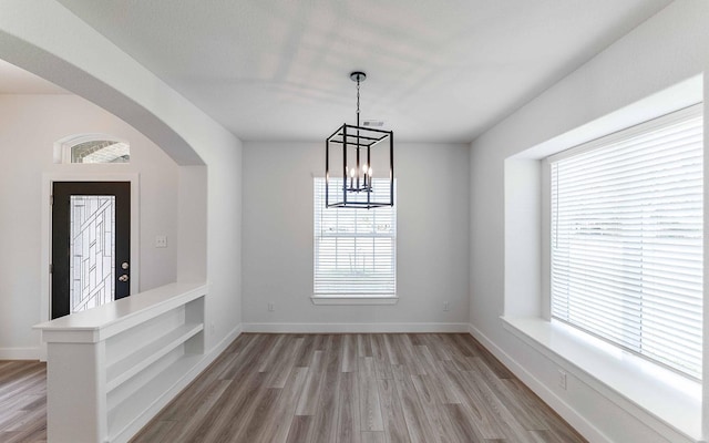 unfurnished dining area featuring an inviting chandelier, light hardwood / wood-style flooring, and a healthy amount of sunlight