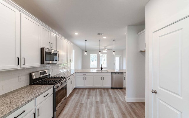 kitchen with kitchen peninsula, stainless steel appliances, sink, white cabinets, and light hardwood / wood-style floors