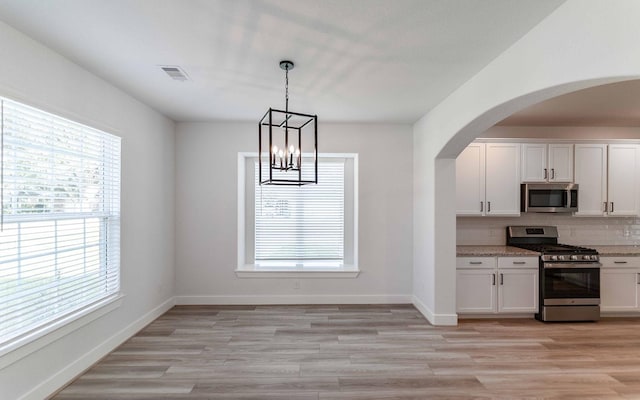 kitchen with white cabinetry, backsplash, appliances with stainless steel finishes, and light hardwood / wood-style flooring