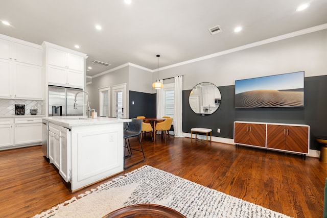 kitchen featuring hanging light fixtures, an island with sink, white cabinets, dark hardwood / wood-style flooring, and ornamental molding