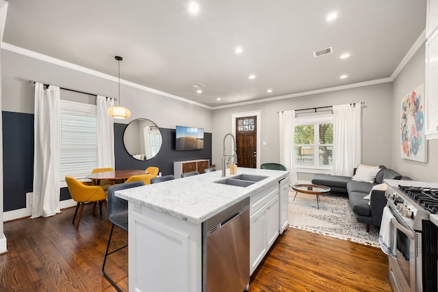 kitchen featuring appliances with stainless steel finishes, dark wood-type flooring, white cabinets, a center island with sink, and sink