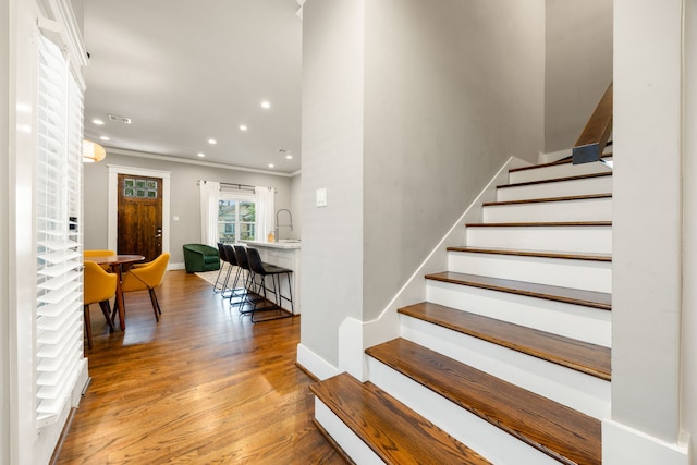 staircase with wood-type flooring, ornamental molding, and sink