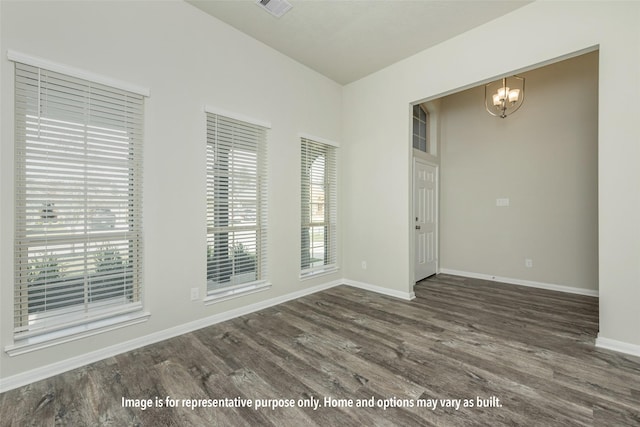 empty room with a notable chandelier, wood finished floors, visible vents, and baseboards