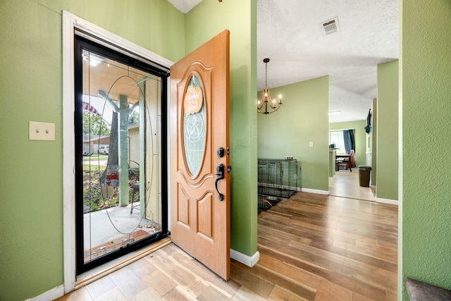 entryway with a textured ceiling, light hardwood / wood-style flooring, and a chandelier