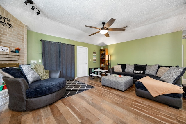 living room featuring a textured ceiling, hardwood / wood-style floors, ceiling fan, and a brick fireplace