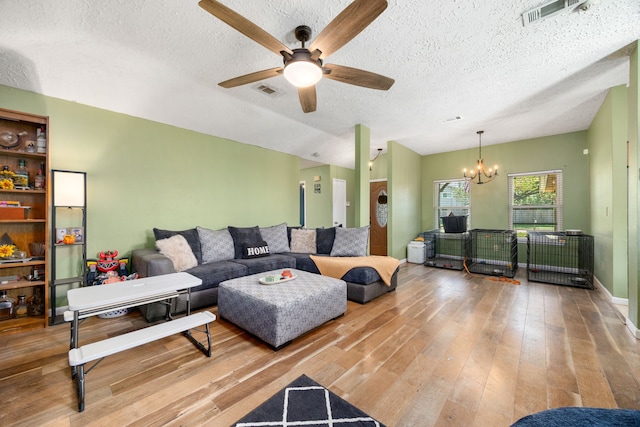 living room with ceiling fan with notable chandelier, wood-type flooring, and a textured ceiling