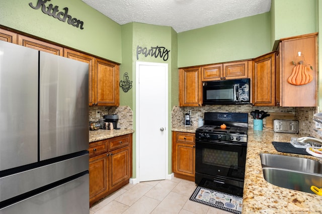 kitchen featuring a textured ceiling, black appliances, sink, and light tile patterned floors