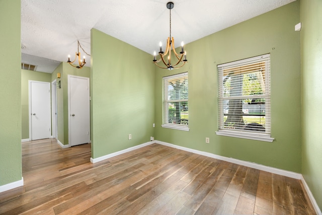 empty room with wood-type flooring, a textured ceiling, and a chandelier