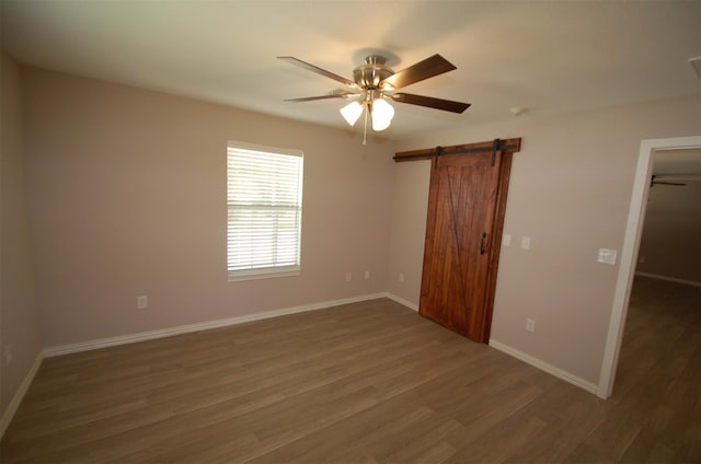 unfurnished bedroom featuring a barn door, dark hardwood / wood-style flooring, ceiling fan, and a closet