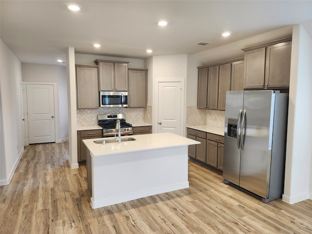 kitchen featuring an island with sink, decorative backsplash, light hardwood / wood-style flooring, and stainless steel appliances