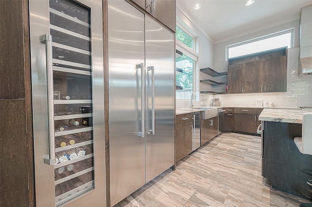 kitchen featuring decorative backsplash, built in refrigerator, light stone counters, dark brown cabinets, and sink