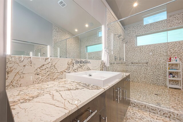 bathroom with a tile shower, ornamental molding, vanity, and tasteful backsplash