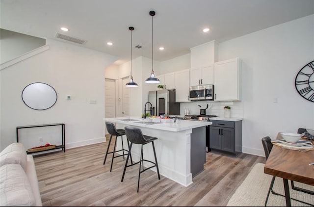 kitchen with gray cabinets, light wood-type flooring, a breakfast bar area, appliances with stainless steel finishes, and decorative light fixtures