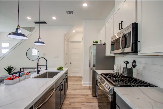 kitchen with appliances with stainless steel finishes, hanging light fixtures, white cabinetry, and sink