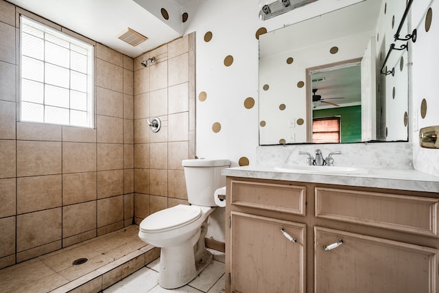 bathroom with tile patterned flooring, tiled shower, ceiling fan, vanity, and toilet