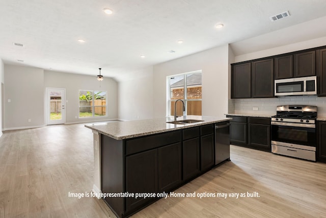 kitchen with sink, tasteful backsplash, a center island with sink, stainless steel appliances, and light hardwood / wood-style floors