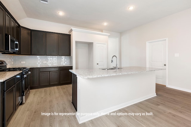 kitchen featuring an island with sink, sink, backsplash, stainless steel appliances, and light hardwood / wood-style floors