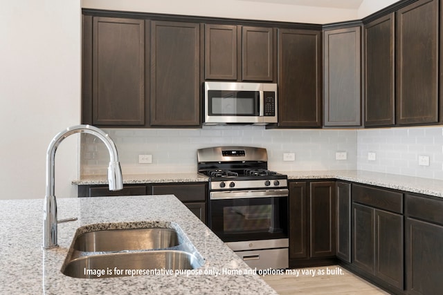 kitchen featuring light stone counters, dark brown cabinetry, sink, appliances with stainless steel finishes, and light wood-type flooring