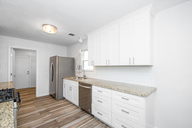 kitchen featuring white cabinets, light stone countertops, sink, stainless steel appliances, and light wood-type flooring