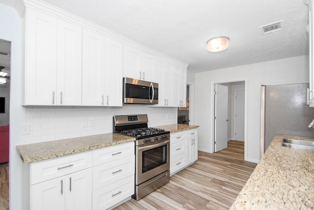 kitchen with white cabinets, light hardwood / wood-style flooring, stainless steel appliances, backsplash, and light stone countertops