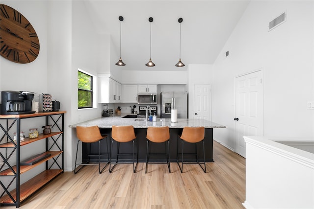 kitchen featuring hanging light fixtures, high vaulted ceiling, white cabinetry, stainless steel appliances, and a breakfast bar