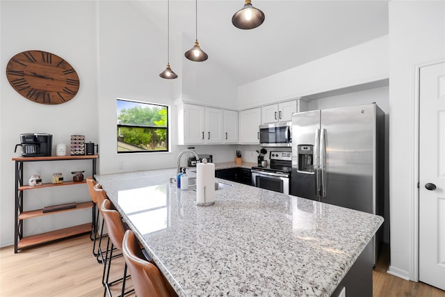 kitchen with white cabinetry, high vaulted ceiling, kitchen peninsula, stainless steel appliances, and light hardwood / wood-style flooring