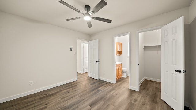 unfurnished bedroom with a closet, dark wood-type flooring, ensuite bath, a walk in closet, and ceiling fan