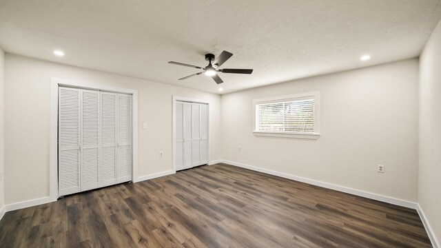 unfurnished bedroom with ceiling fan, multiple closets, and dark wood-type flooring