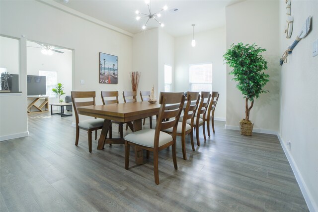 dining space with ceiling fan with notable chandelier, a towering ceiling, and dark wood-type flooring