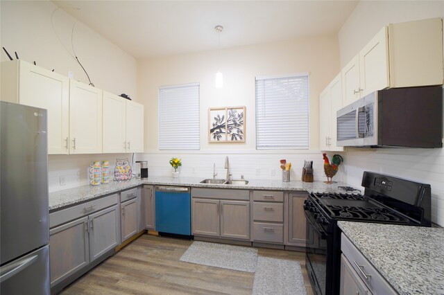 kitchen featuring light stone counters, sink, wood-type flooring, decorative light fixtures, and stainless steel appliances